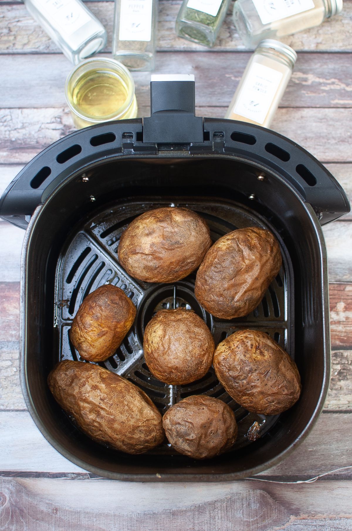 cooked potatoes in the air fryer next to oil in a glass and spices in glass containers