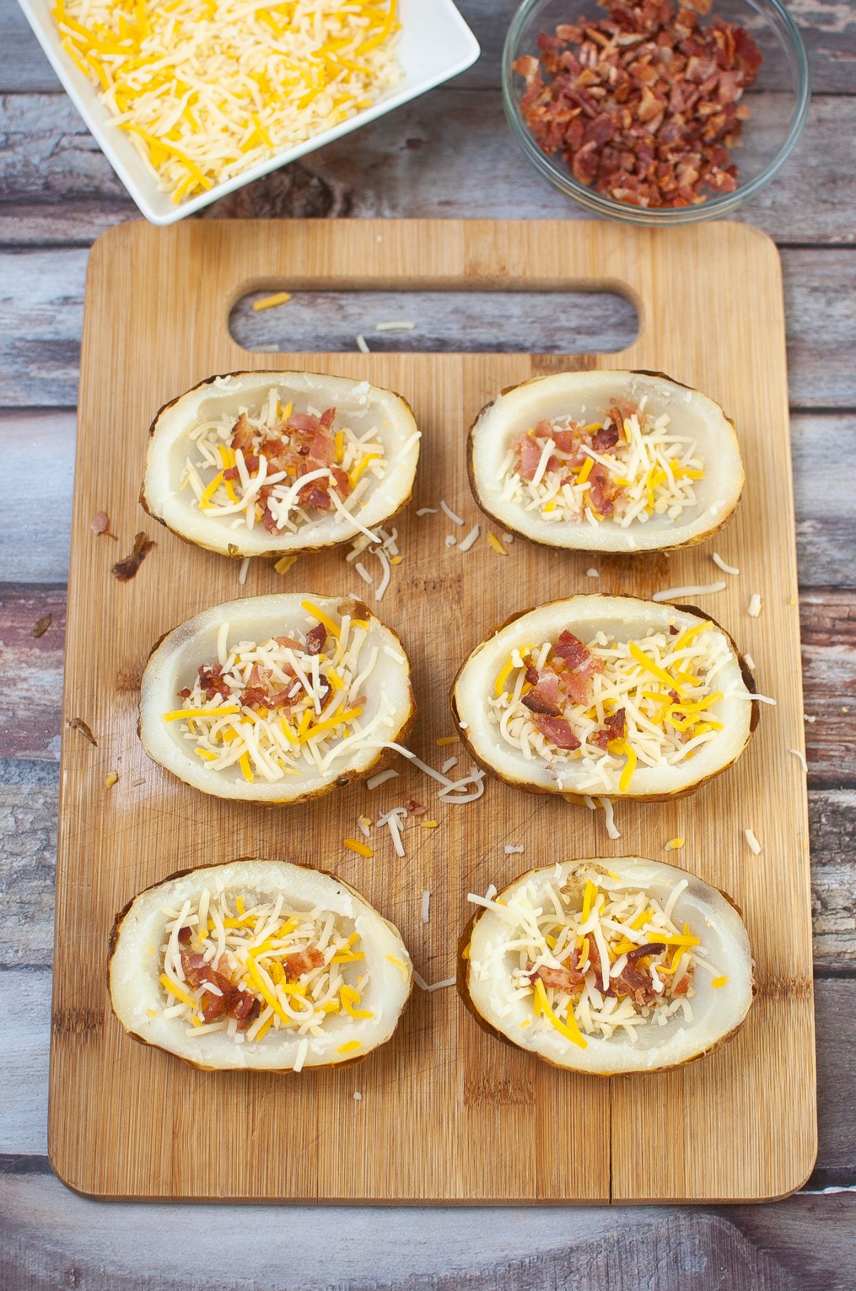 baked potato halves Topped with bacon, cheese, and spices with more bacon and cheese in the background