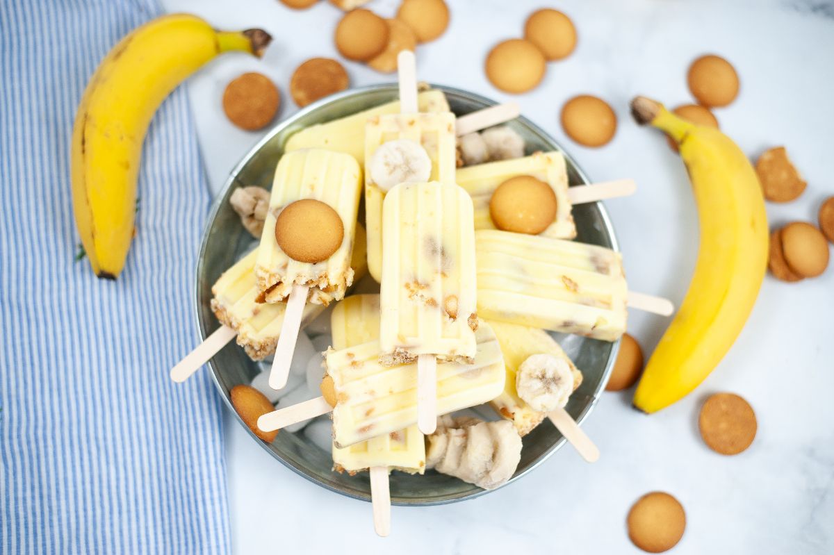 Banana Pudding Popsicles in a large bowl on ice, with vanilla wafters and bananas on the side