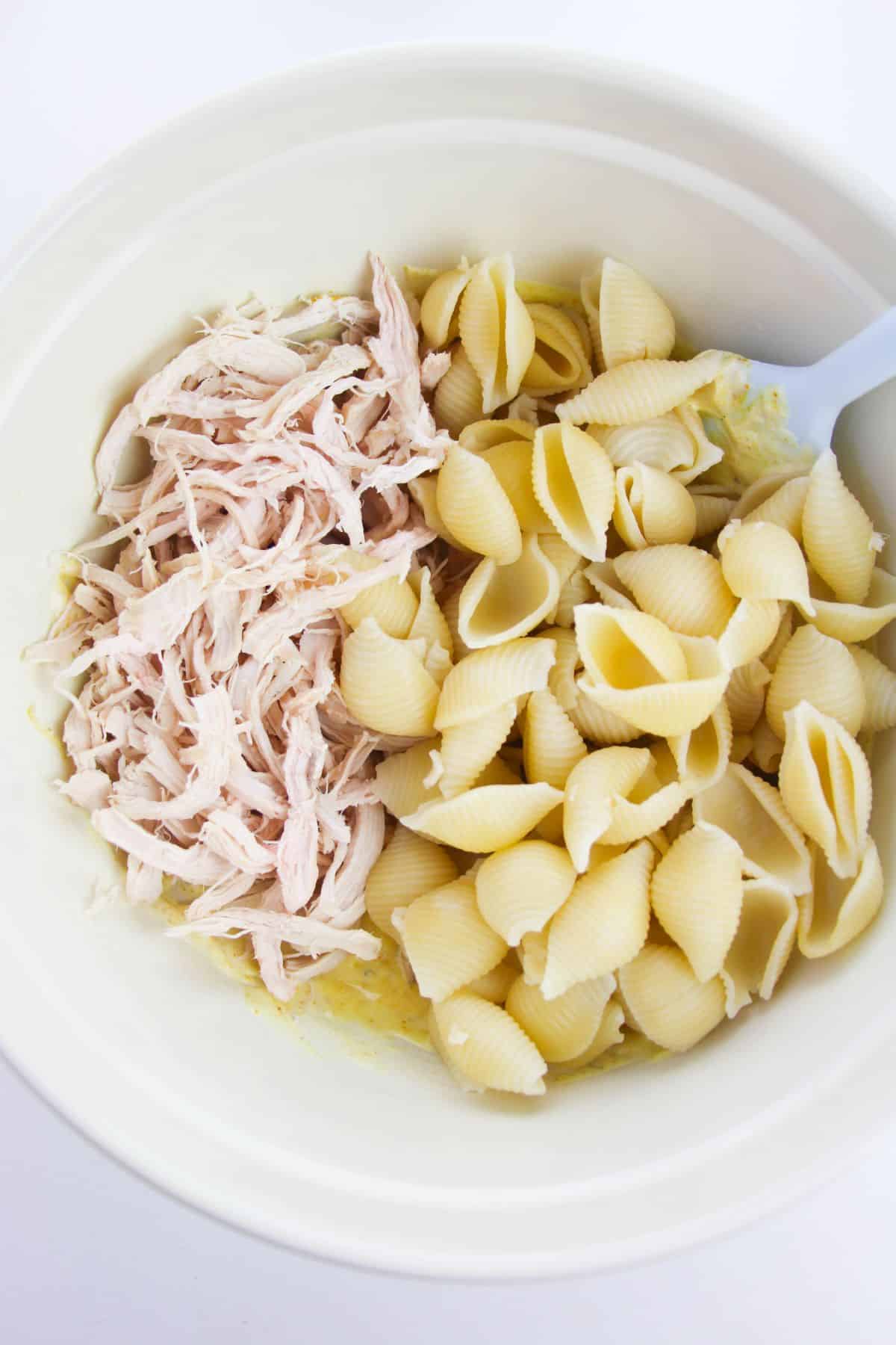 cooked pasta and chicken added to the dressing mixture in a bowl