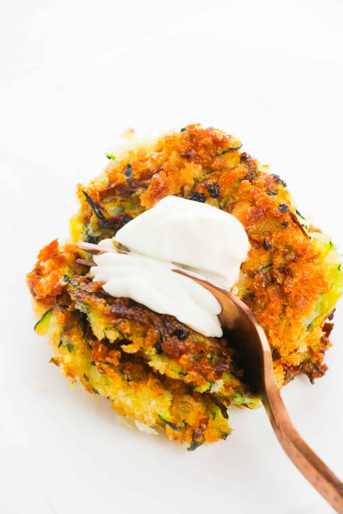a closeup of Crispy Zucchini Fritters with sauce and a fork