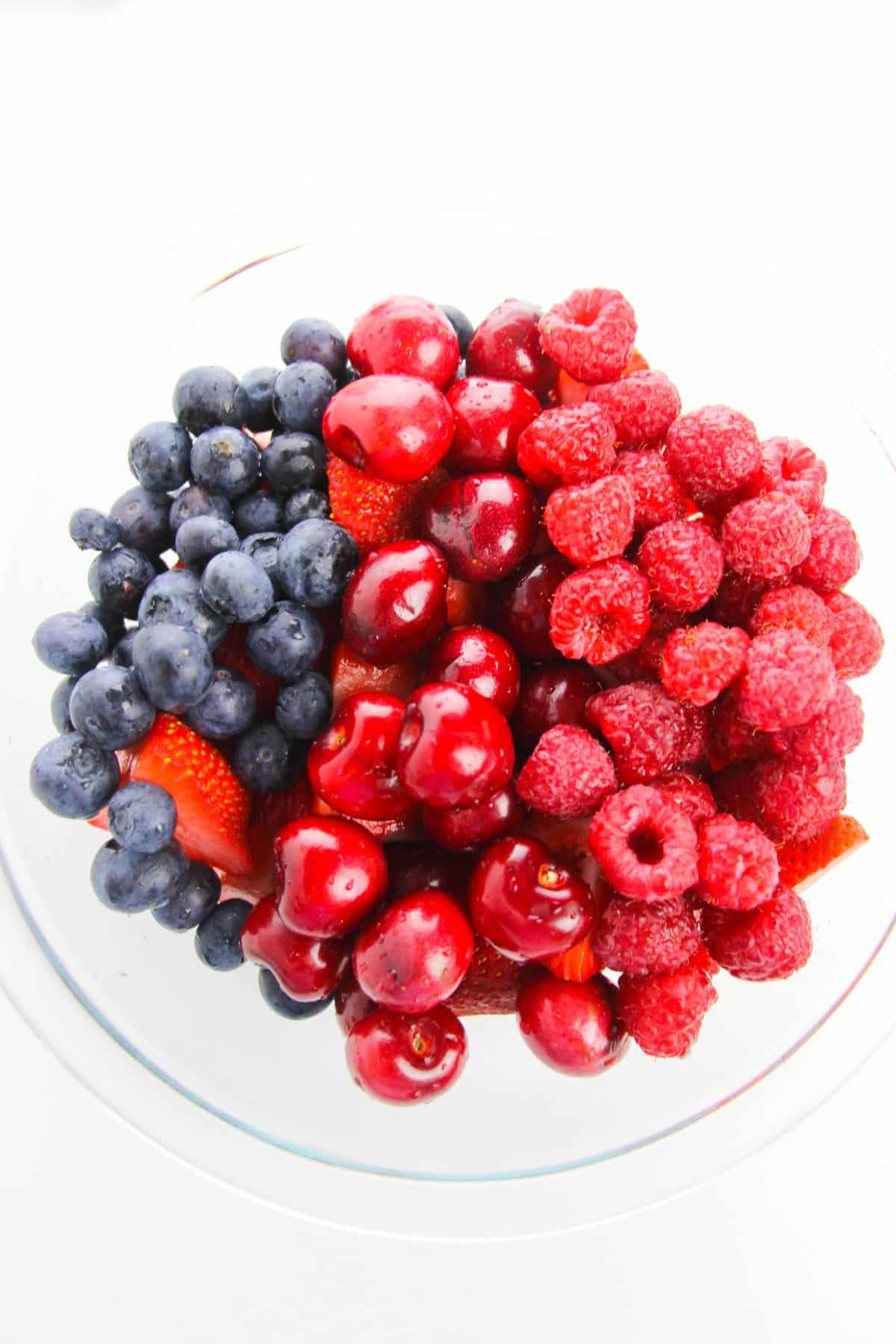 Cherries, raspberries, and blueberries in a large glass mixing bowl