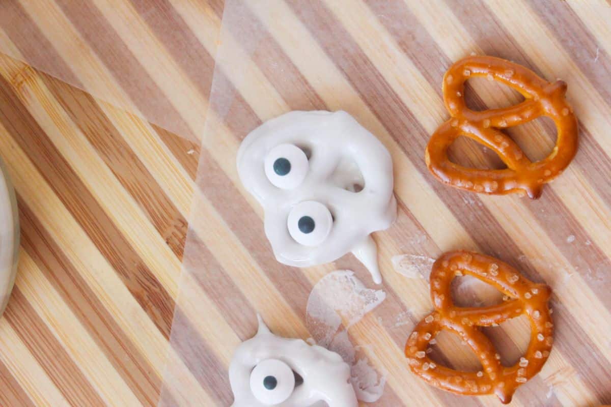 White candy-coated pretzels with candy eyes and 2 plain pretzels on a piece of wax paper