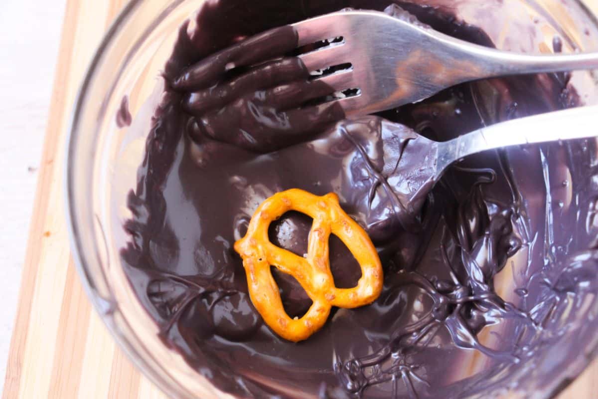 a pretzel being dipped into the melted black candy