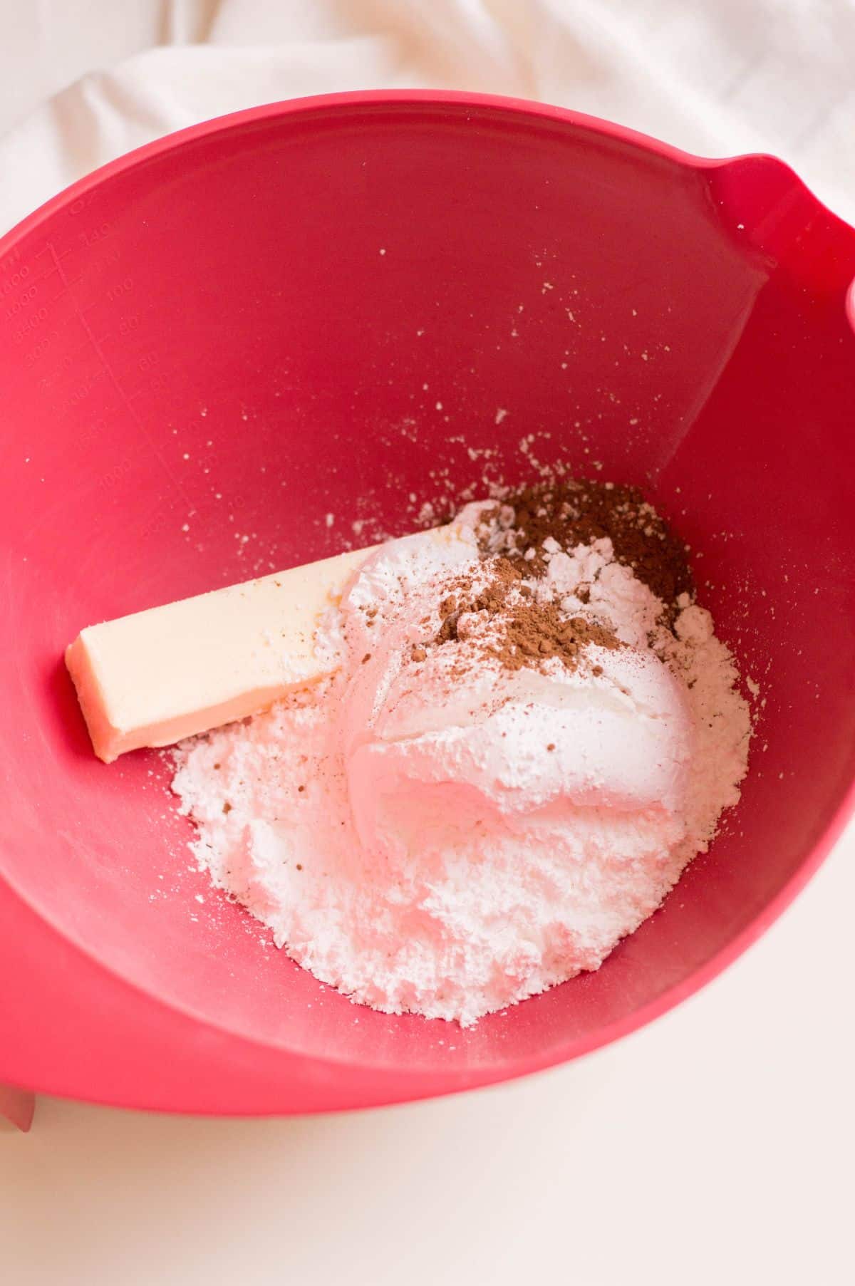Butter, confectioners’ sugar, cocoa powder, and milk in a large red bowl.