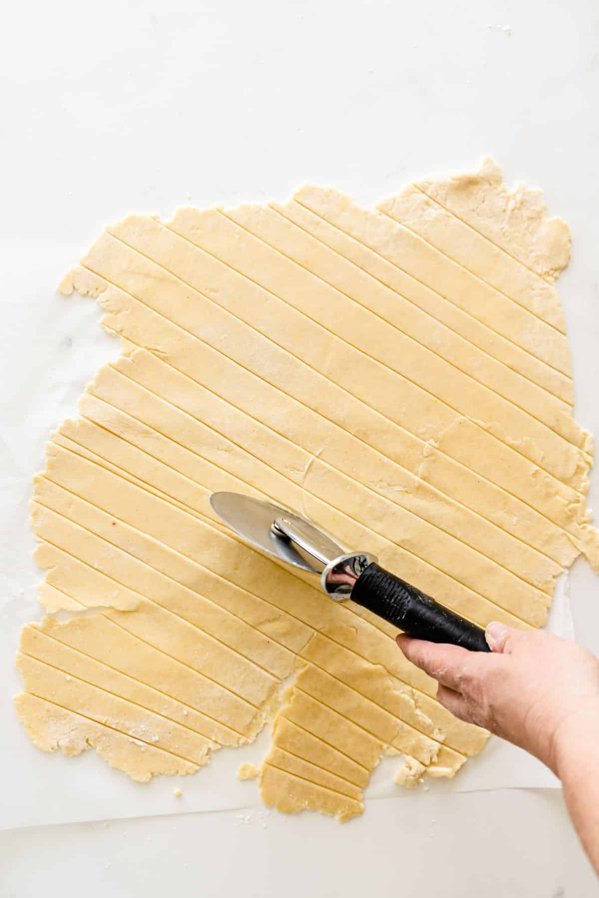 a hand using a pizza cutter to cut strips of crust to form a lattice-style top for the pie