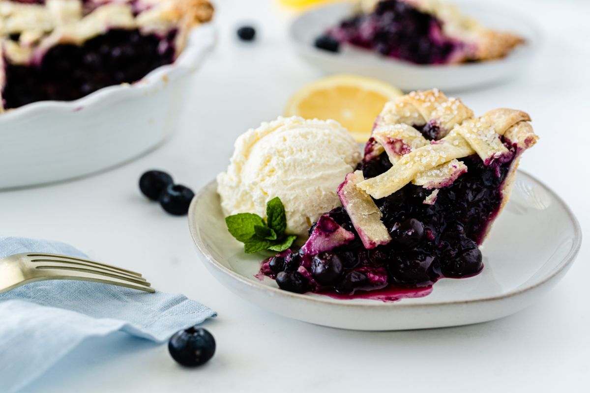 Sliced homemade Fresh Blueberry Pie on a plate with ice cream on the side