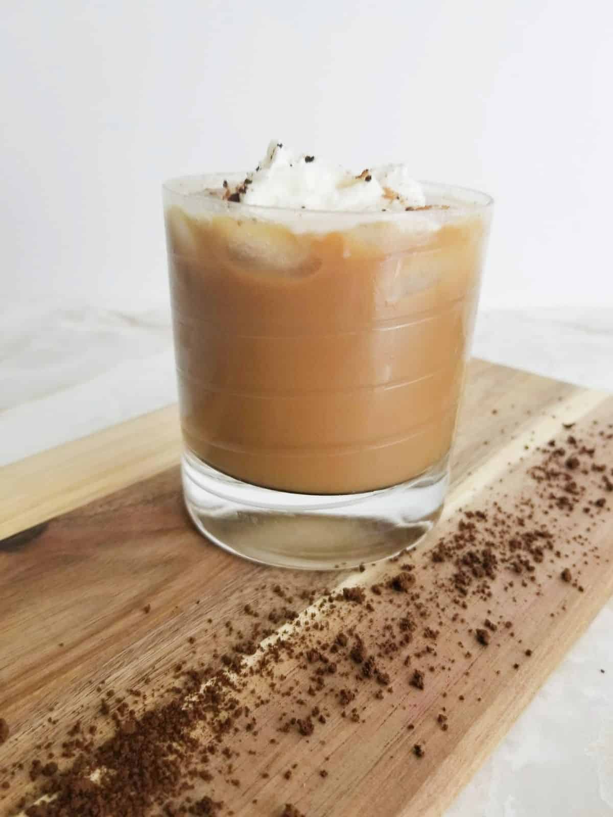 Iced Coffee topped with whipped cream and cinnamon in a glass on a wooden board.