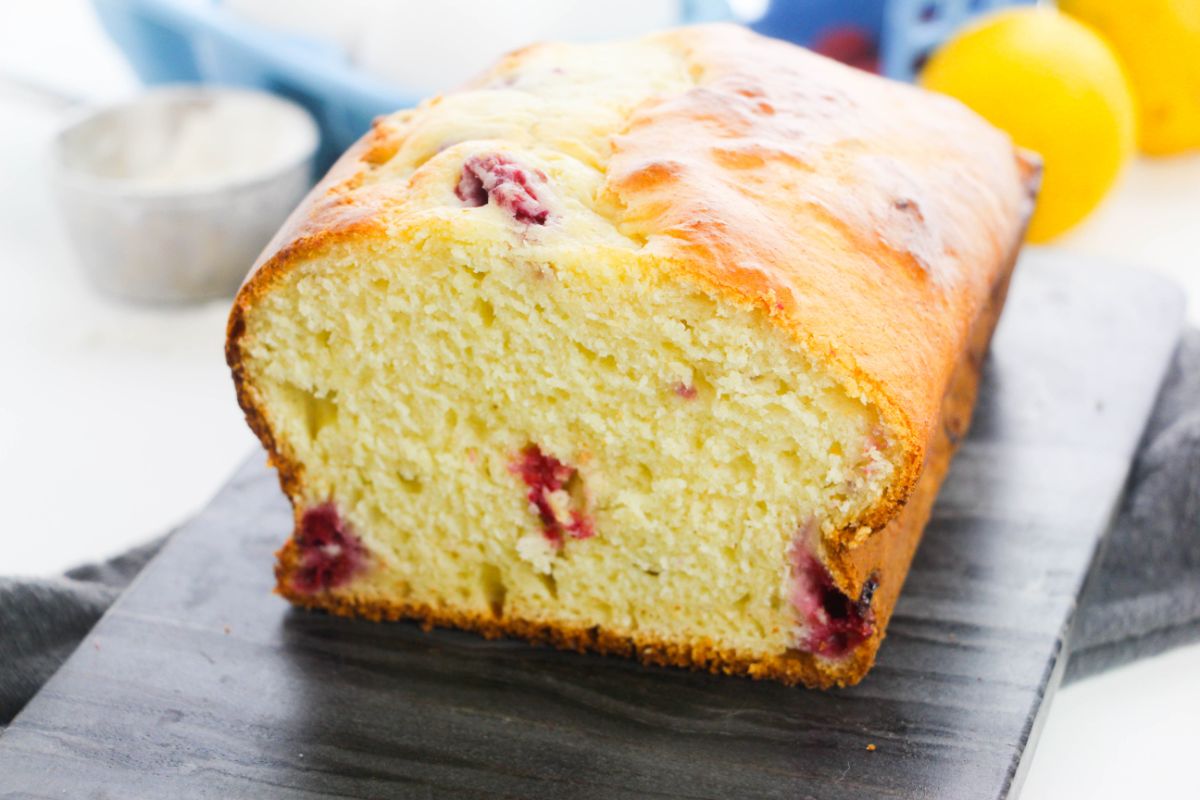 Lemon Raspberry Loaf on a wooden plate with flour, lemon and raspberries on the side