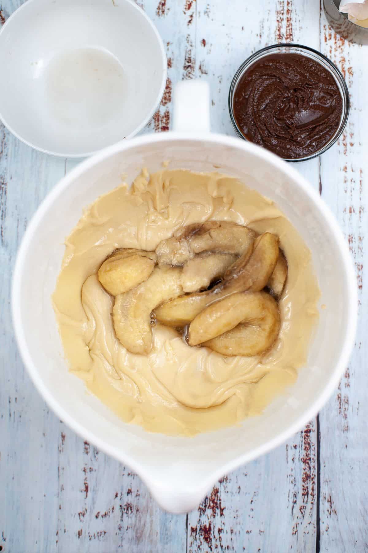 mashed bananas in a bowl of batter next to nutella in a glass bowl and an empty white bowl