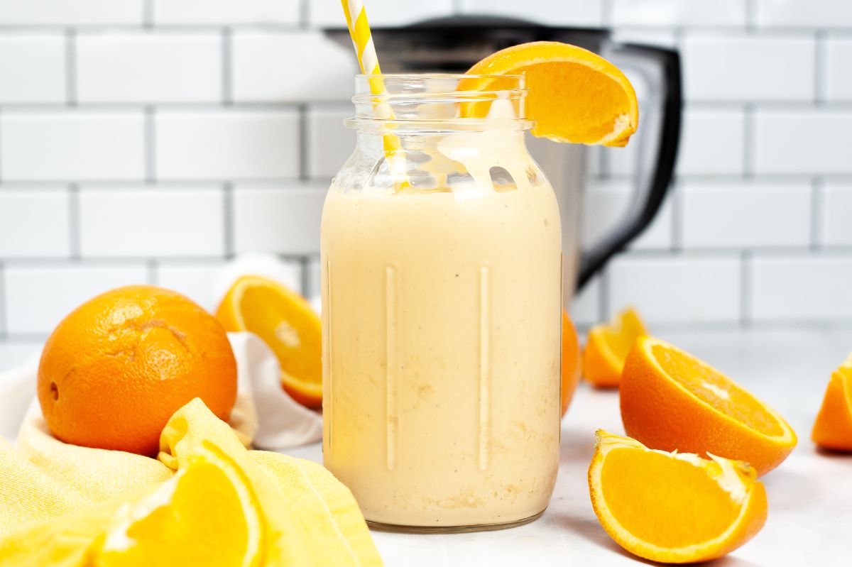Orange Milkshake in a jar with straw and orange slice and surrounded by oranges and halved oranges