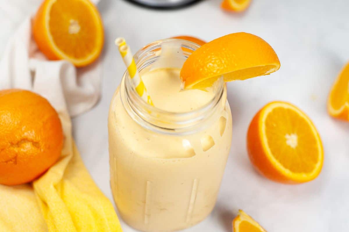 Orange Milkshake in a jar with a straw and orange slice with orange halves around it