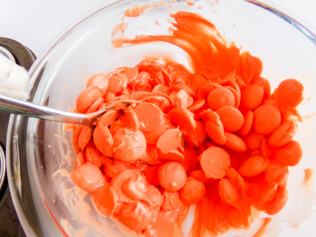 Orange candy melts and a spoon in a microwave safe bowl.