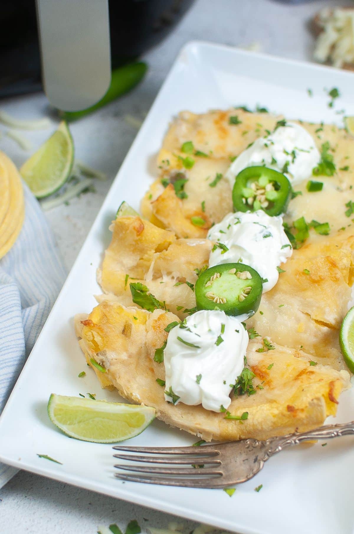 Air Fryer Cheese Enchiladas on a plate garnished with sour cream, green onions, and cilantro.
