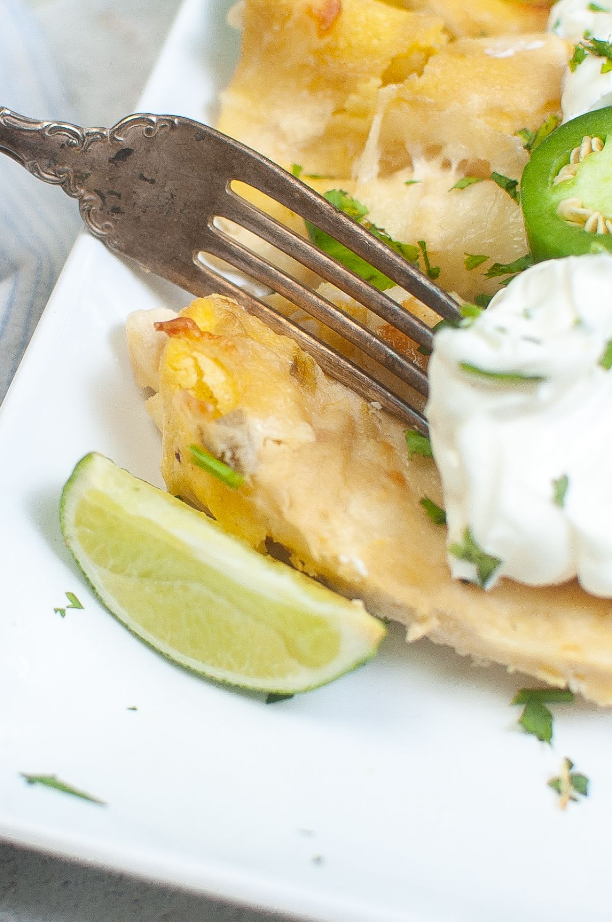 closeup of a fork on Air Fryer Cheese Enchiladas on a plate garnished with sour cream, green onions, and cilantro.