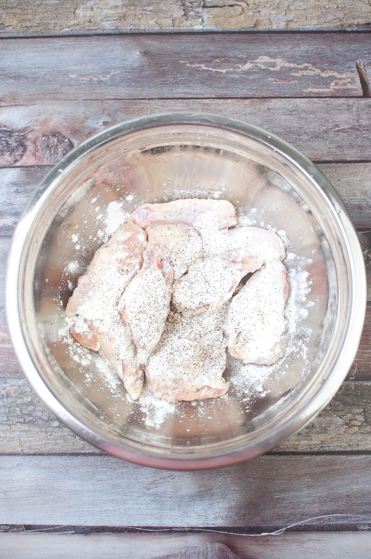 Chicken wings in a large bowl with cornstarch, salt and pepper.