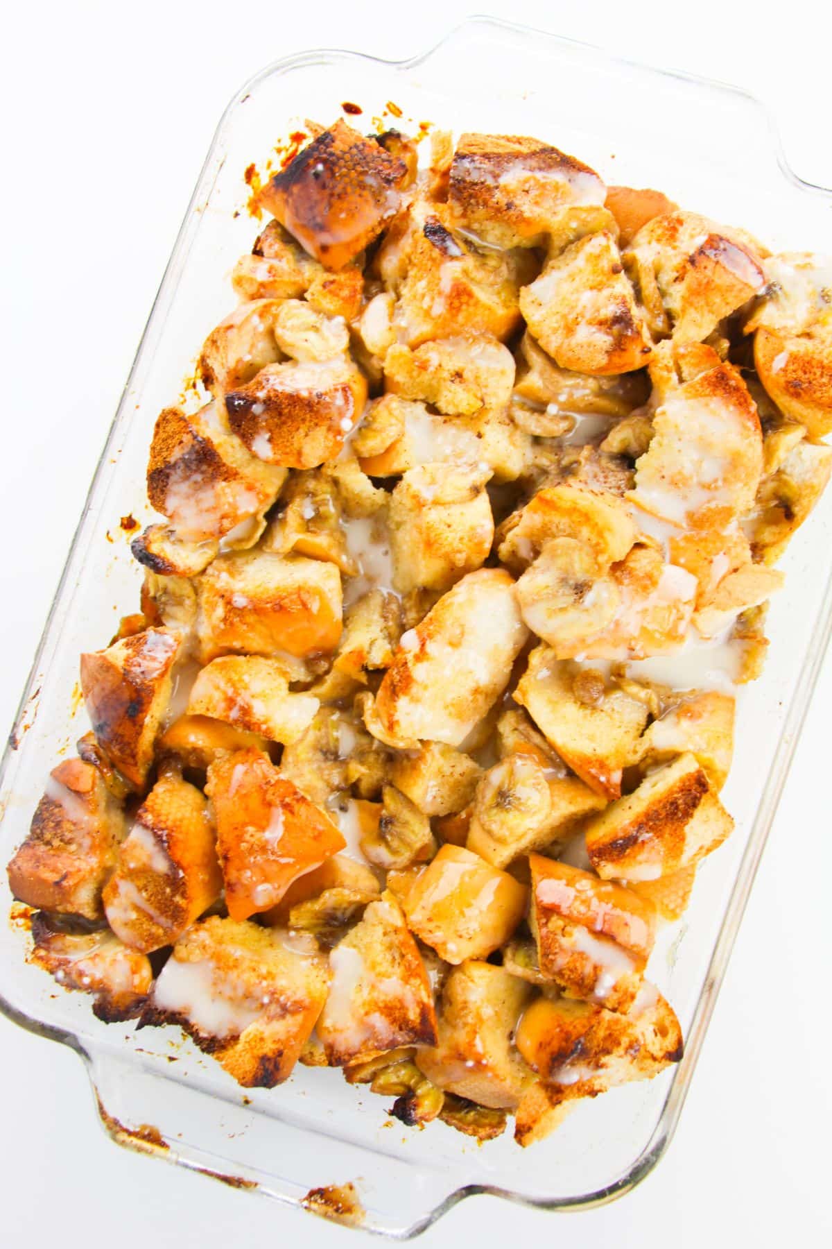Banana bread pudding with glaze in a glass baking dish.