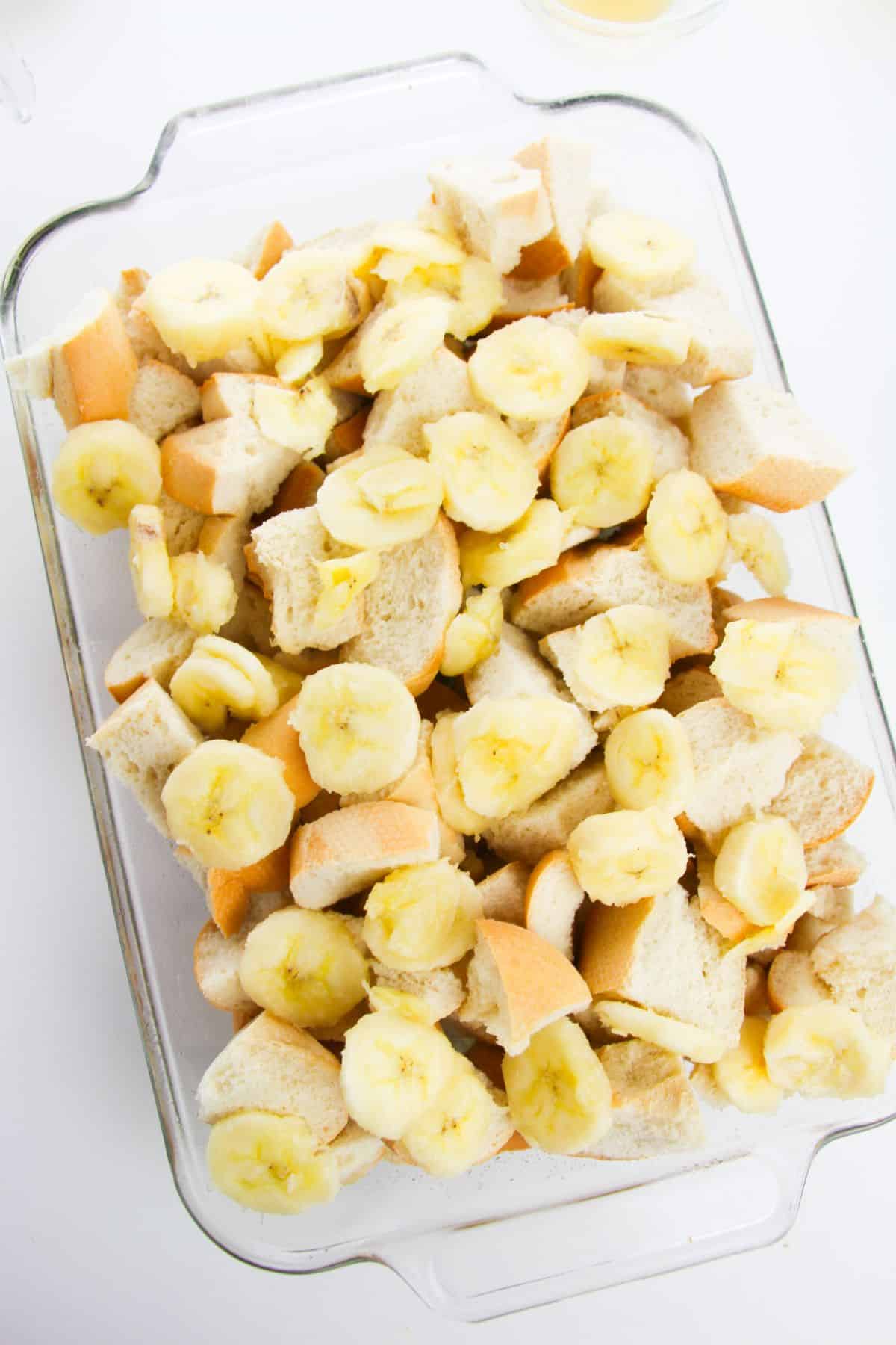 Bread cubes and banana slices in a glass baking dish.