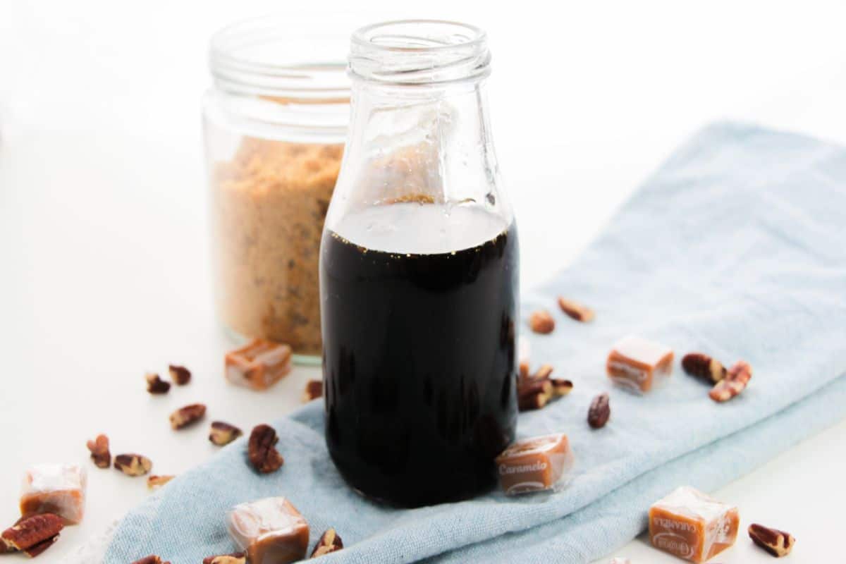 Caramel Pecan Syrup in a bottle with brown sugar and pecans on the side.