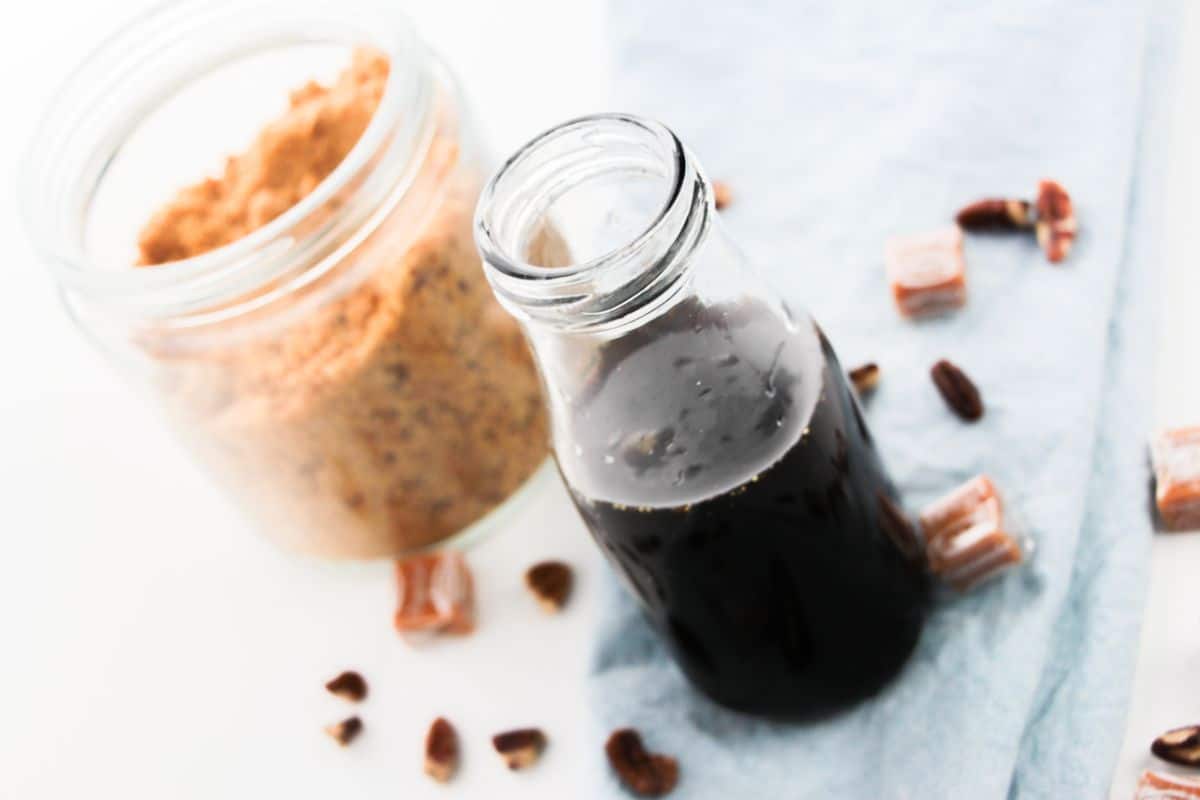 Caramel Pecan Syrup in a bottle with brown sugar and pecans on the side.