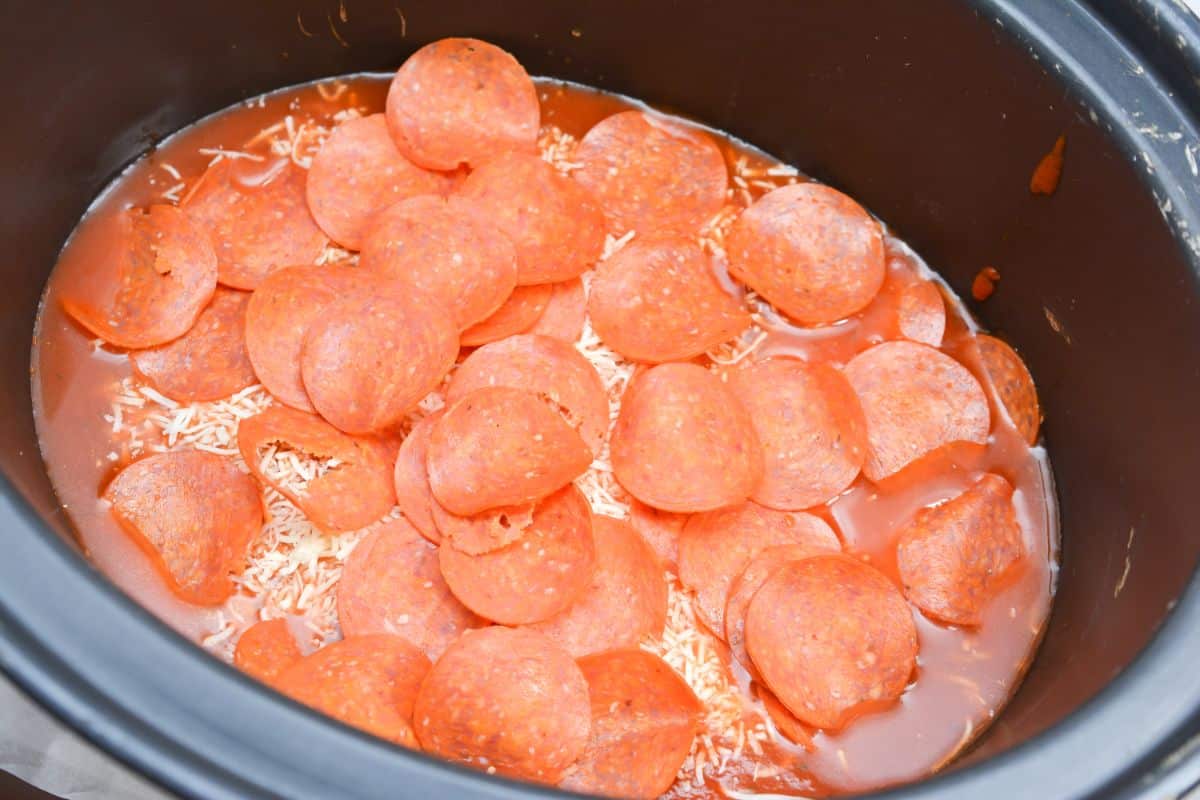 Pasta sauce, water, pepperoni slices, and mozzarella cheese inside the crockpot.