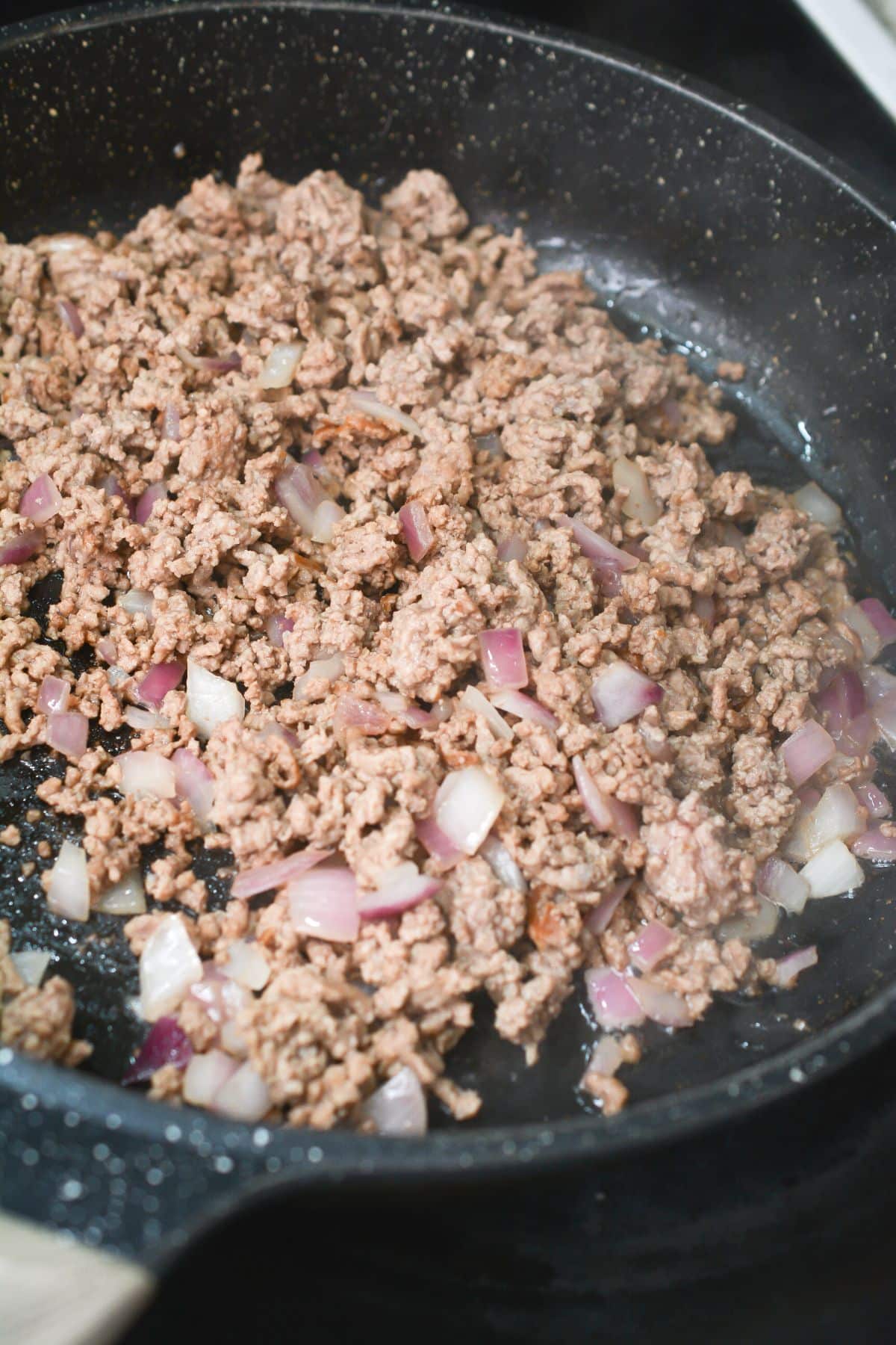 Ground beef and onions are being sautéed in the skillet.
