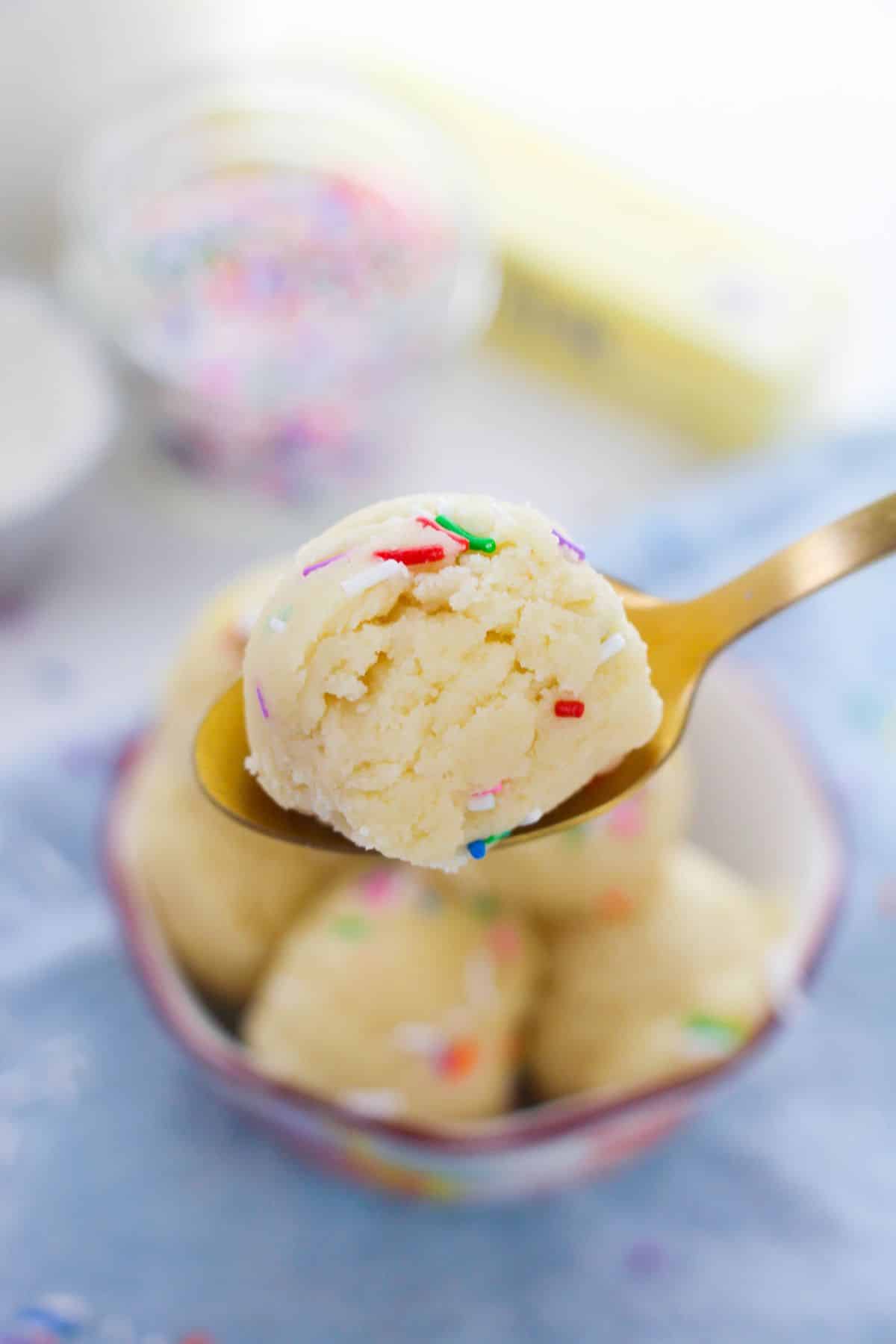a closeup of Edible Sugar Cookie Dough with sprinkles on a spoon with more cookie dough blurred underneath.