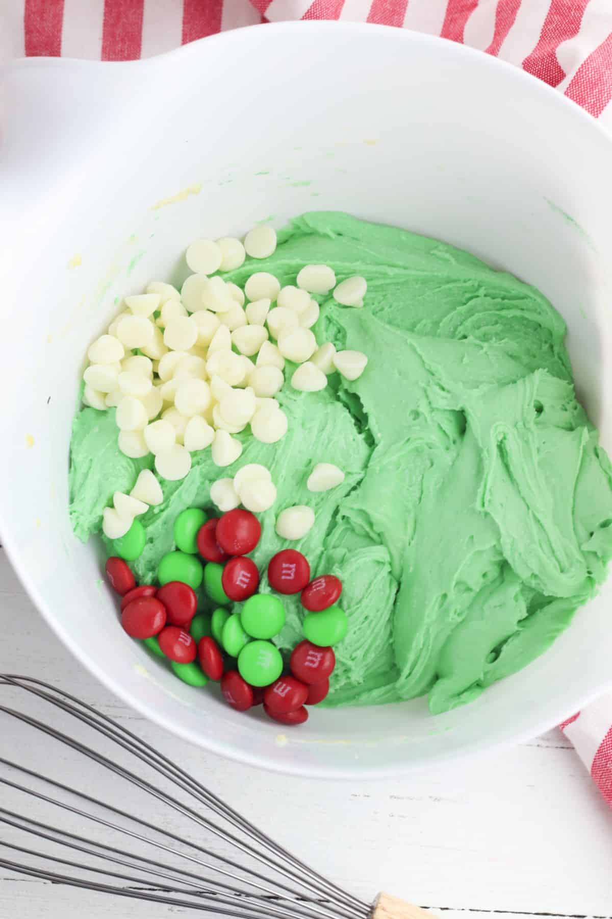 Dough mixture with white chocolate chips  and M&Ms in a mixing bowl.