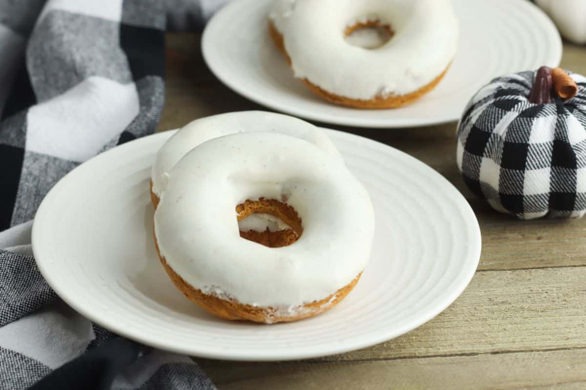 Pumpkin Cake Doughnuts on a plate next to a black and white fabric pumpkin with more doughnuts on a plate in the background