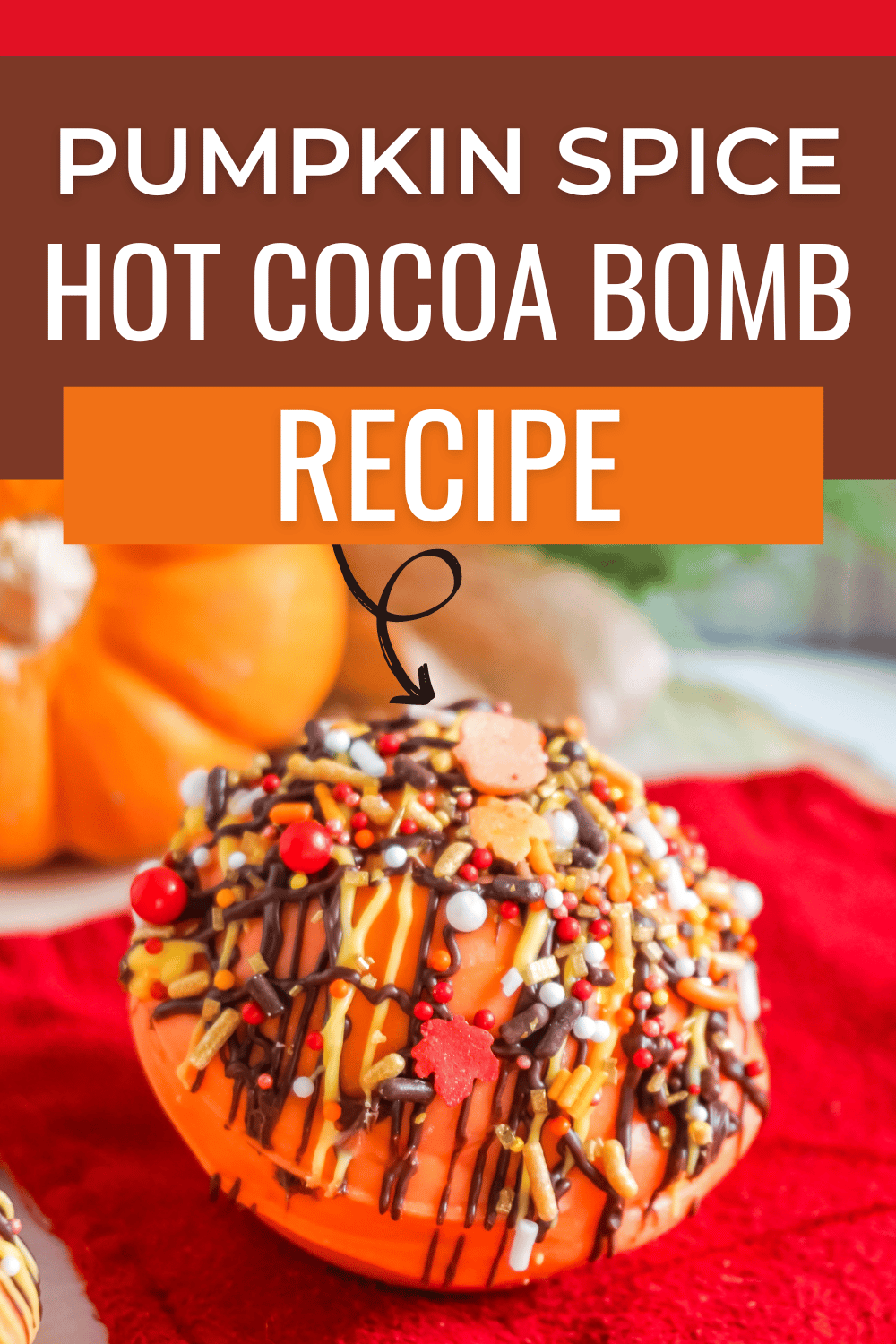 a closeup of a hot cocoa bomb on a red cloth with a pumpkin in the background with title text reading Pumpkin Spice Hot Cocoa Bomb Recipe