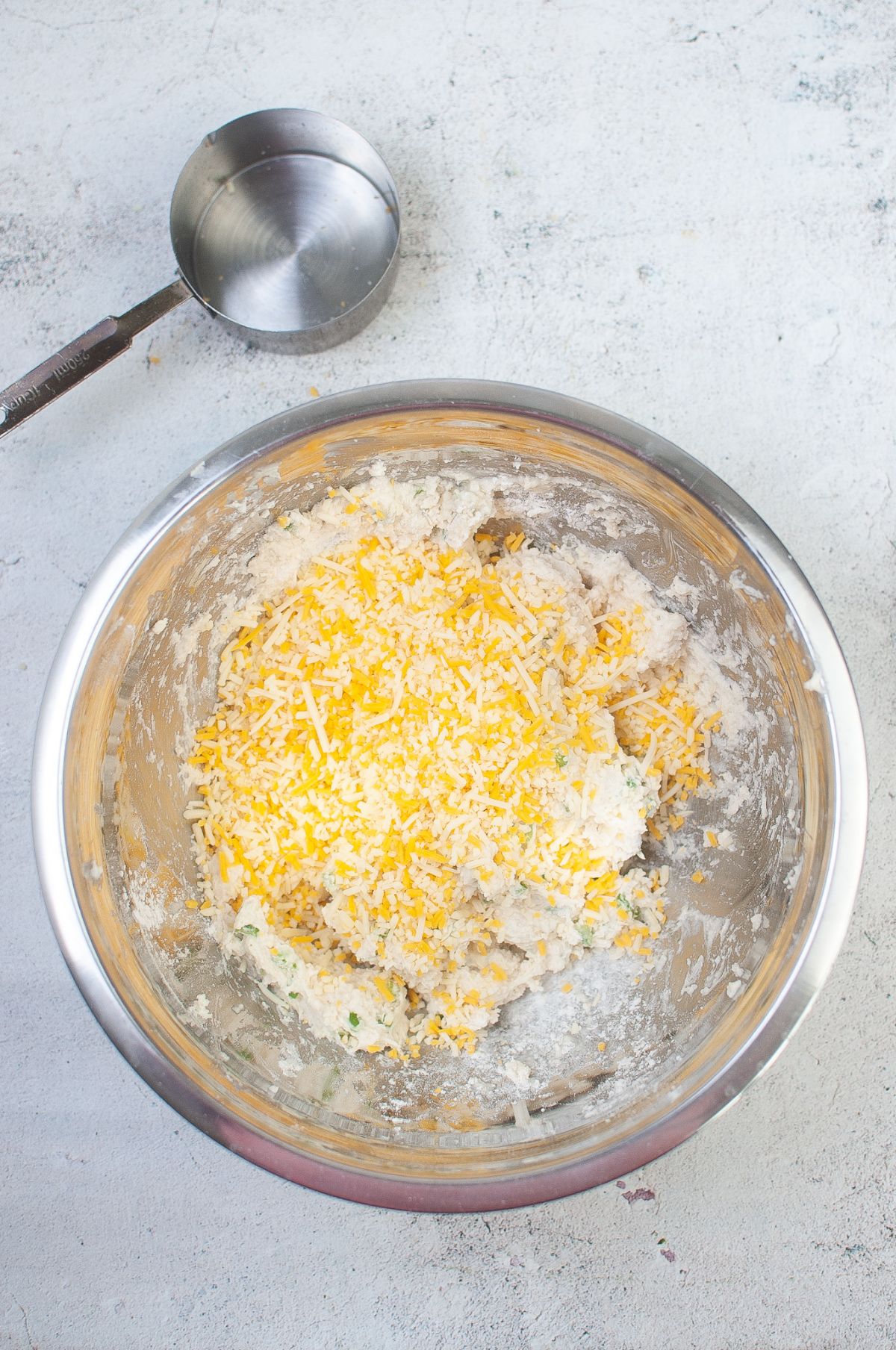 The shredded cheese is added to the mixture in a metal bowl.