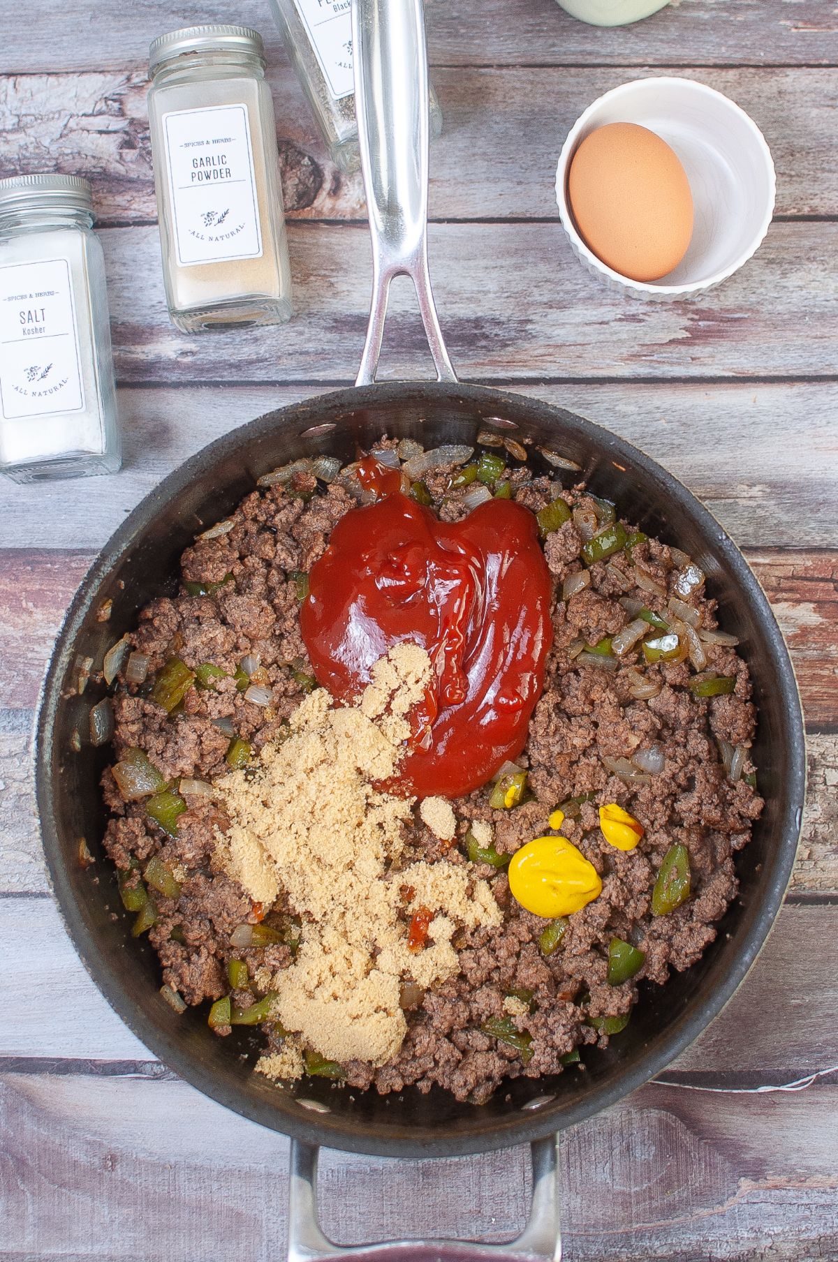 The mustard, brown sugar, and ketchup are being added to the meat mixture in the pan.