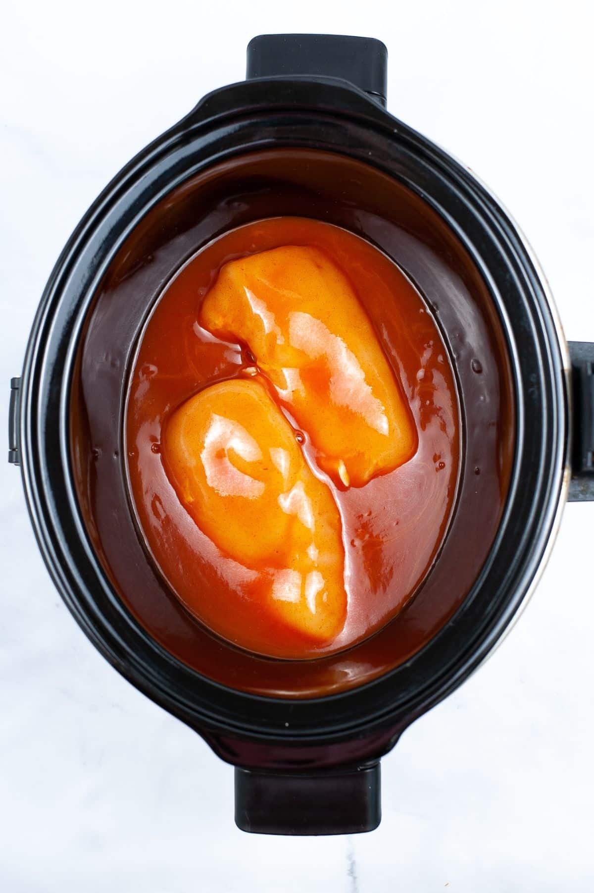 Chicken breasts and enchilada sauce inside the crock pot.