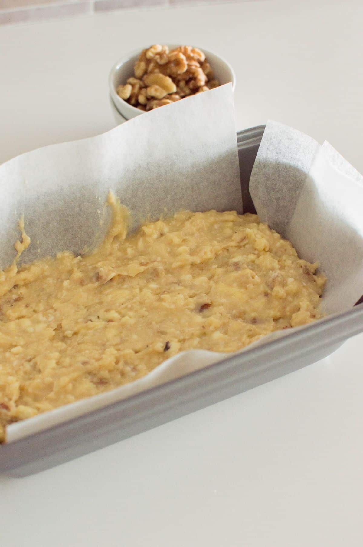 maple walnut bread batter on parchment paper in the loaf pan.