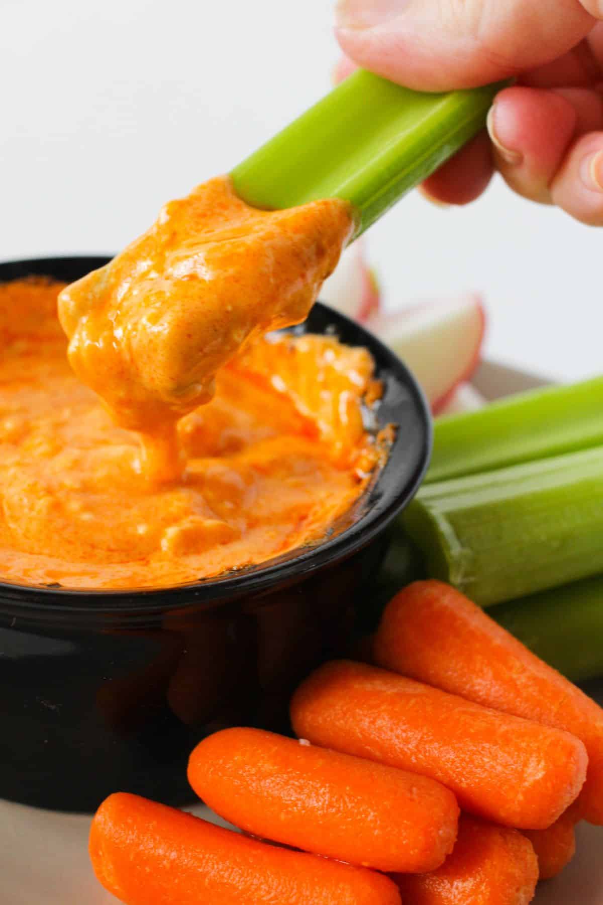 The celery is being dipped in the Slow Cooker Buffalo Chicken Dip with vegetables on the side.
