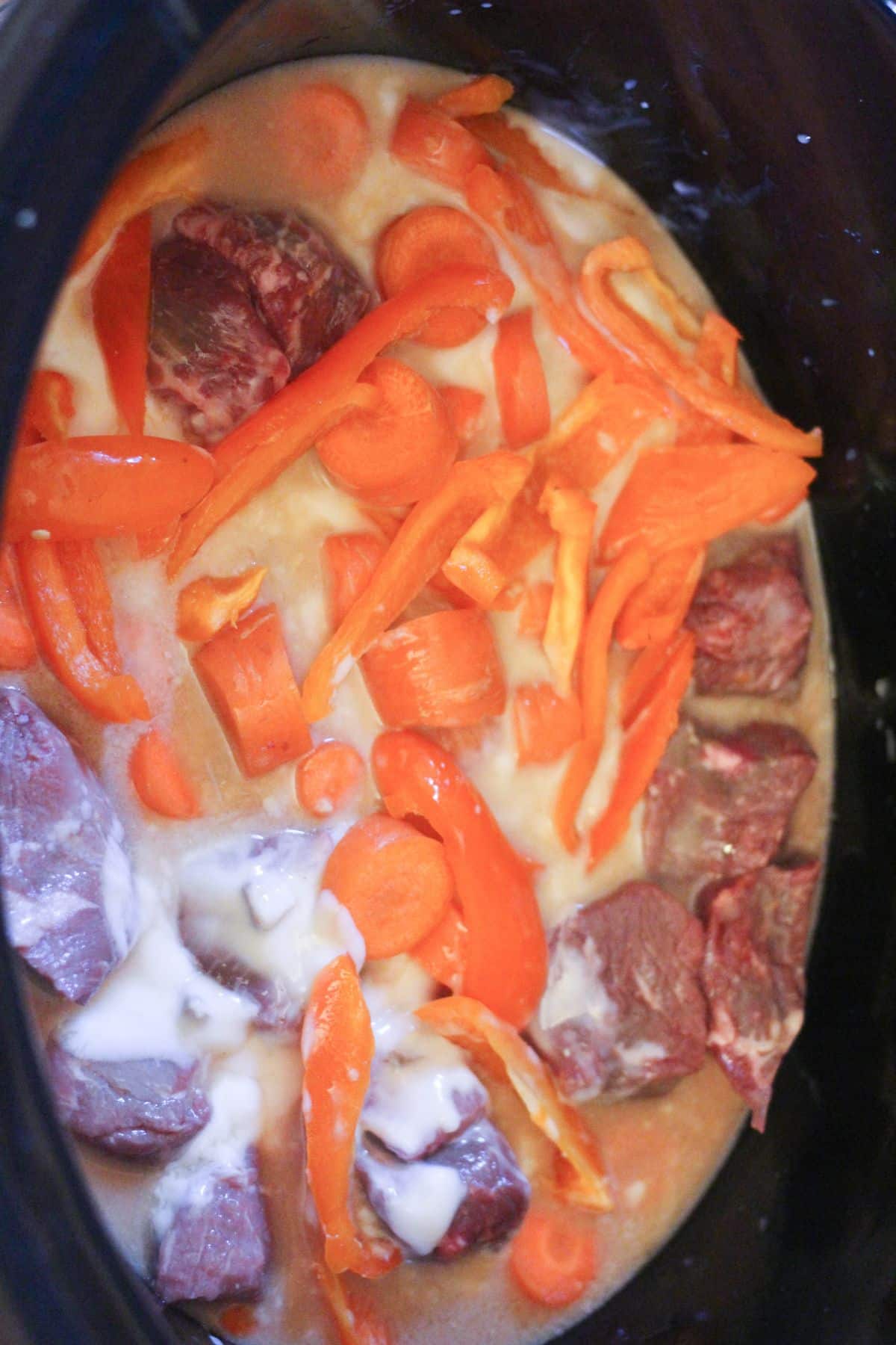 beef stew meat, vegetables and sauce in a crock pot.