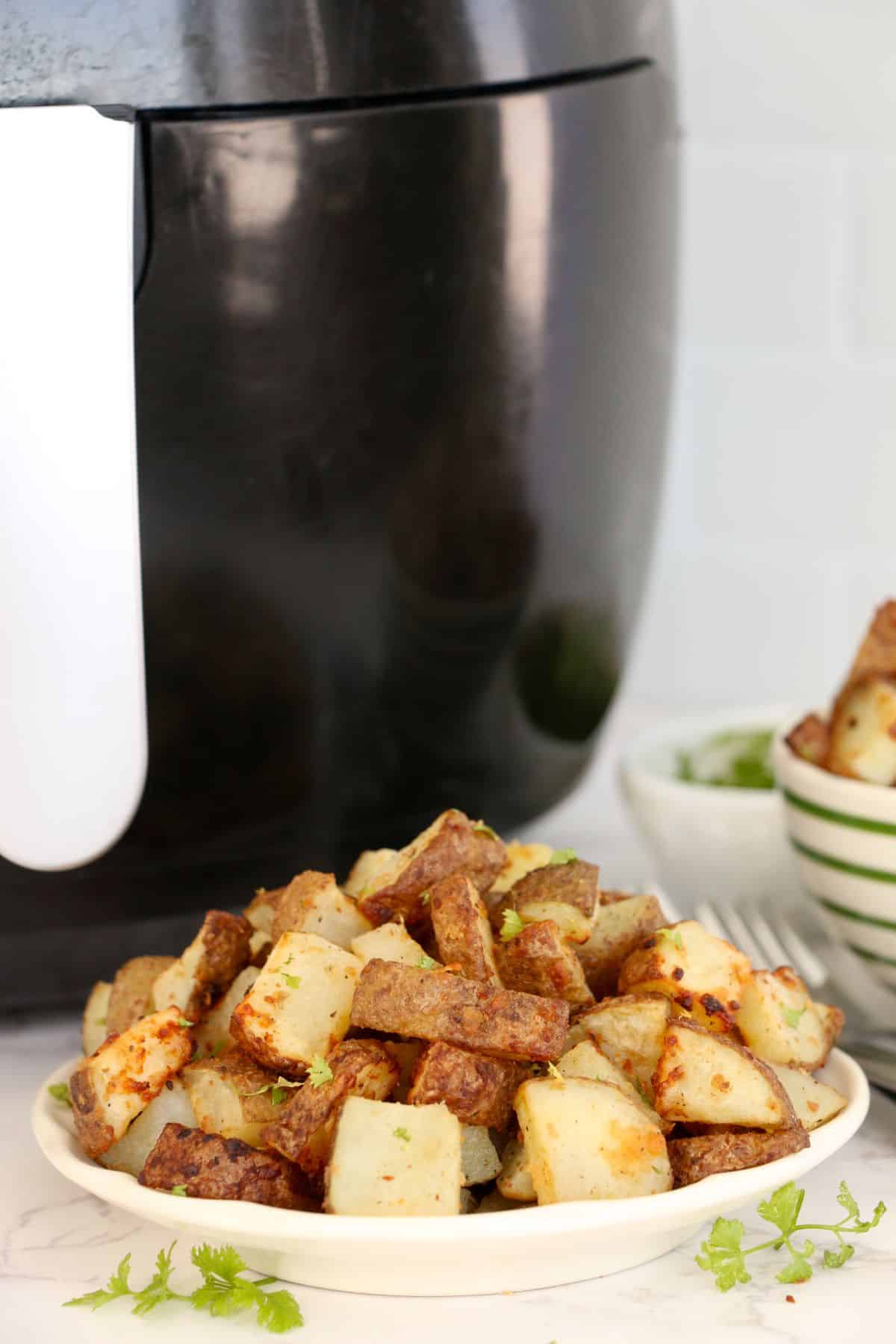 Air Fryer Diced Potatoes on a serving plate, with Air Fryer on the side.