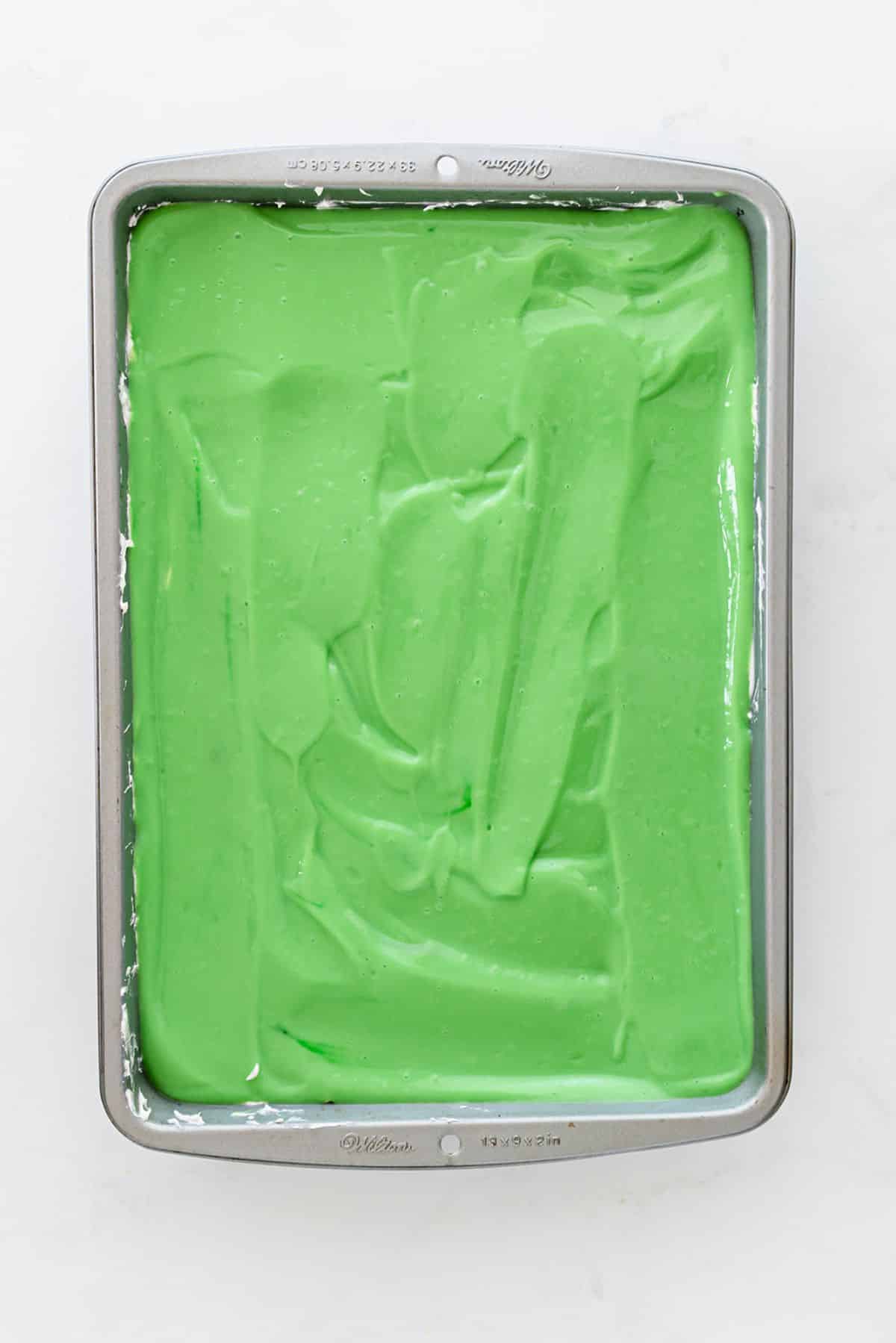 A layer of green pudding is spread over the cream cheese layer.