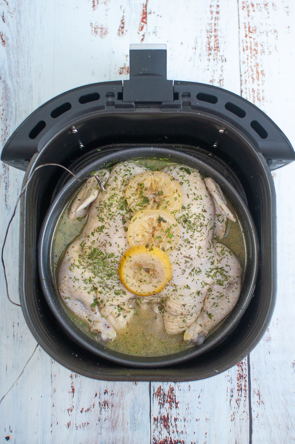 Marinated chicken in a pan inside the Air Fryer topped with sliced lemon.