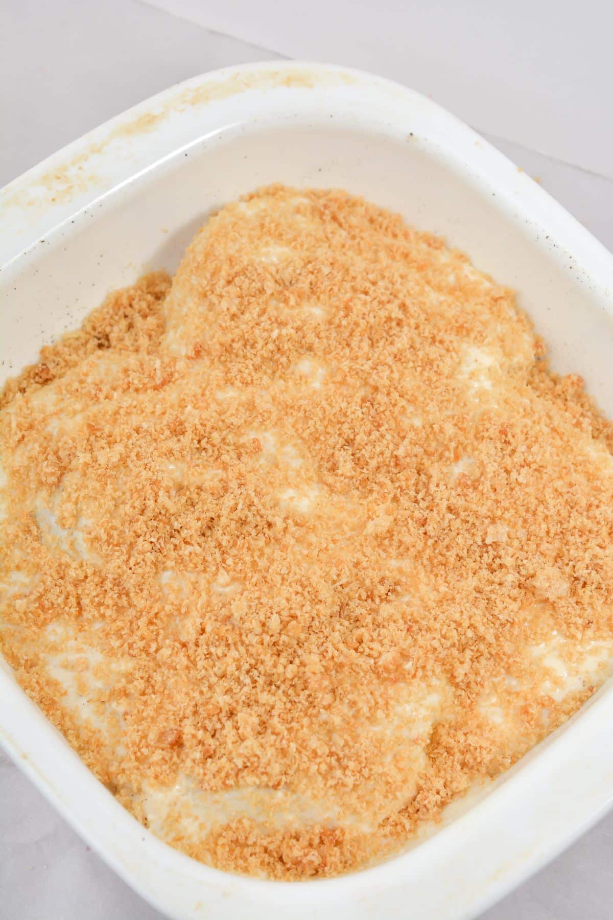 A layer of pork rind crumbs covers the chicken in a baking dish.