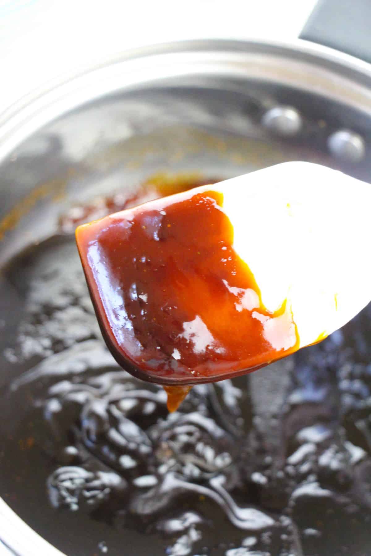 Sauce mixture in a small saucepan with spoon coated with sauce above the pan.