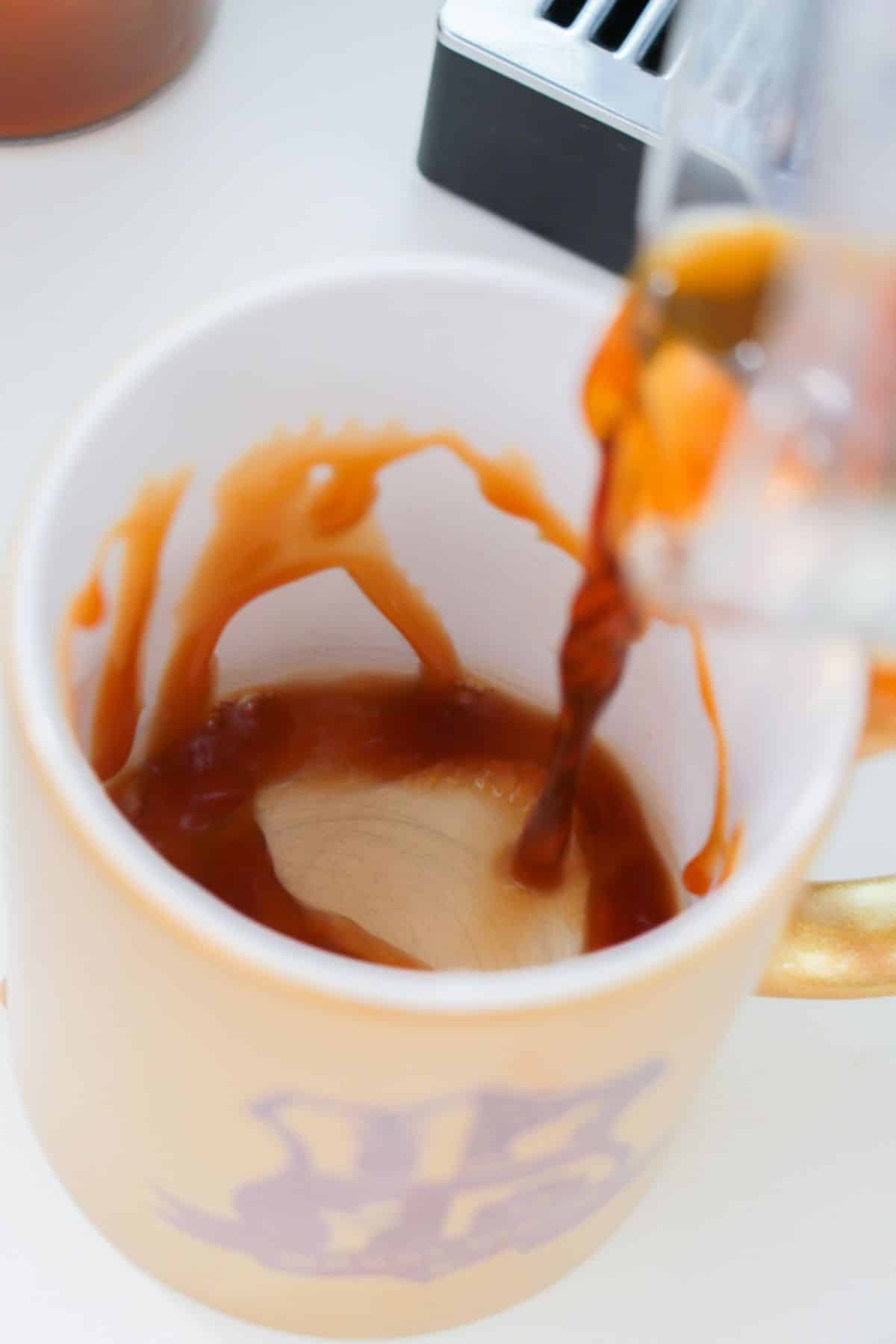 The caramel sauce is being drizzled into the mug.