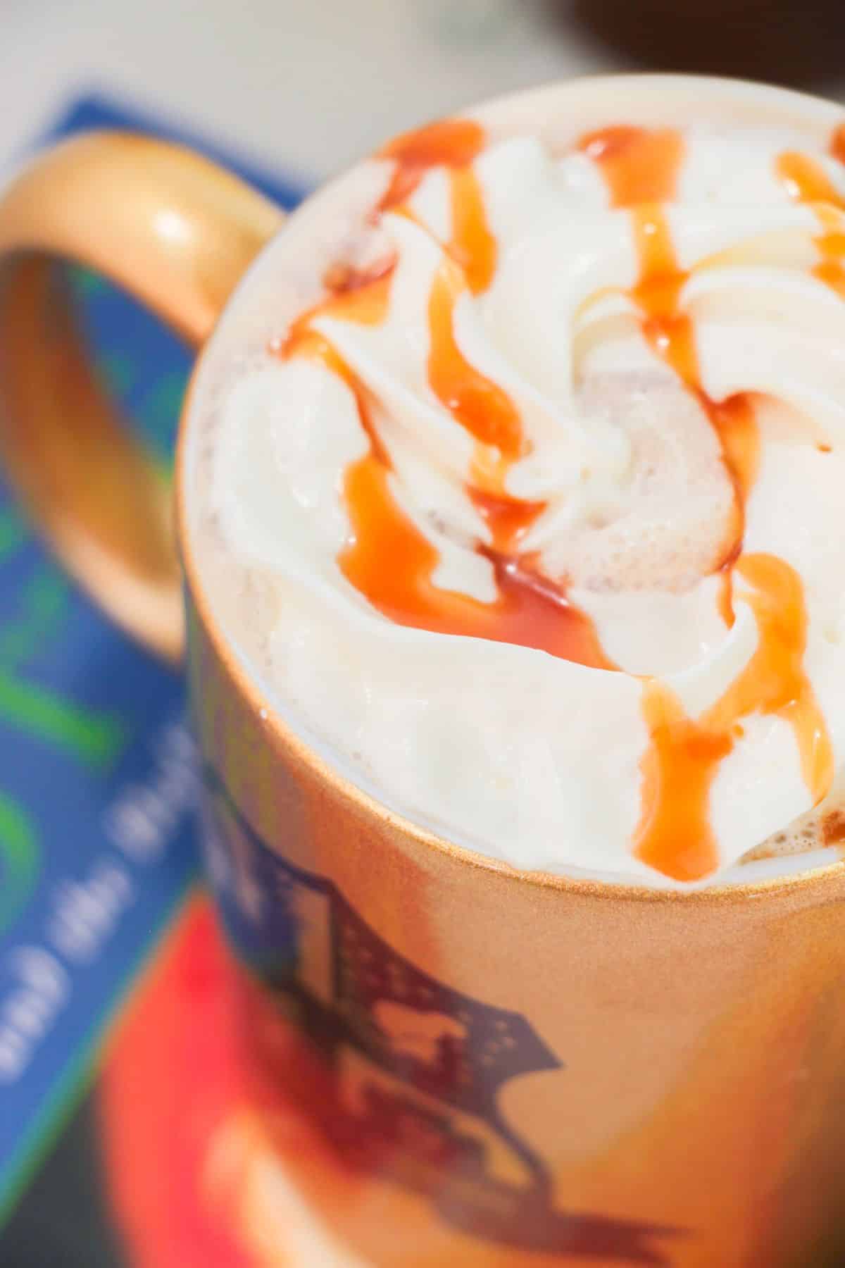 a closeup of Butterbeer Latte in a mug with caramel drizzle on the top.
