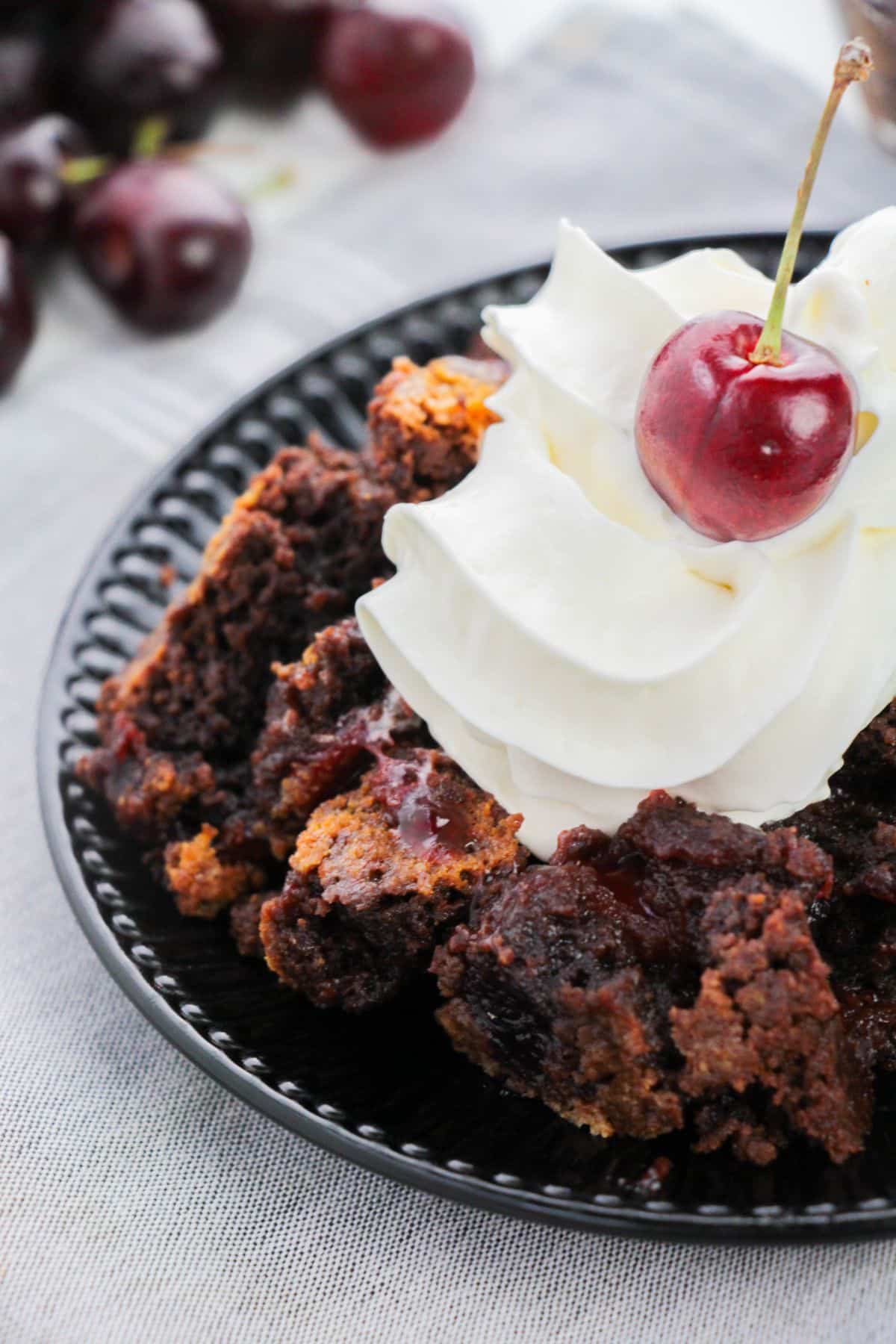 Chocolate Cherry Cobbler on a serving plate with whipped cream and cherry on the top.