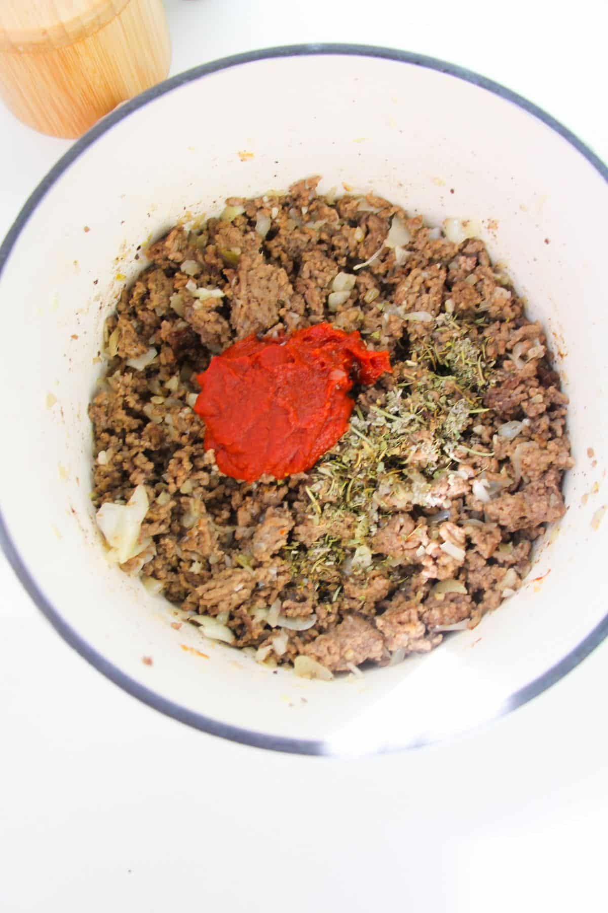 Tomato paste and seasoning are added to the meat mixture.