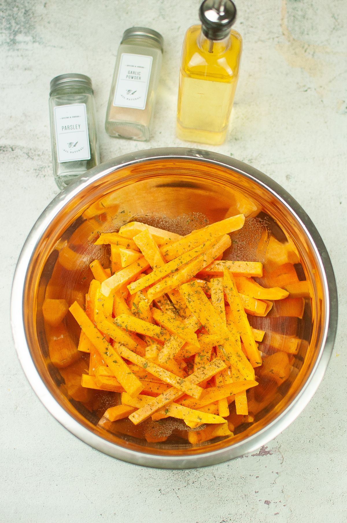 Squash fries in a mixing bowl, seasoned with garlic powder and parsley.