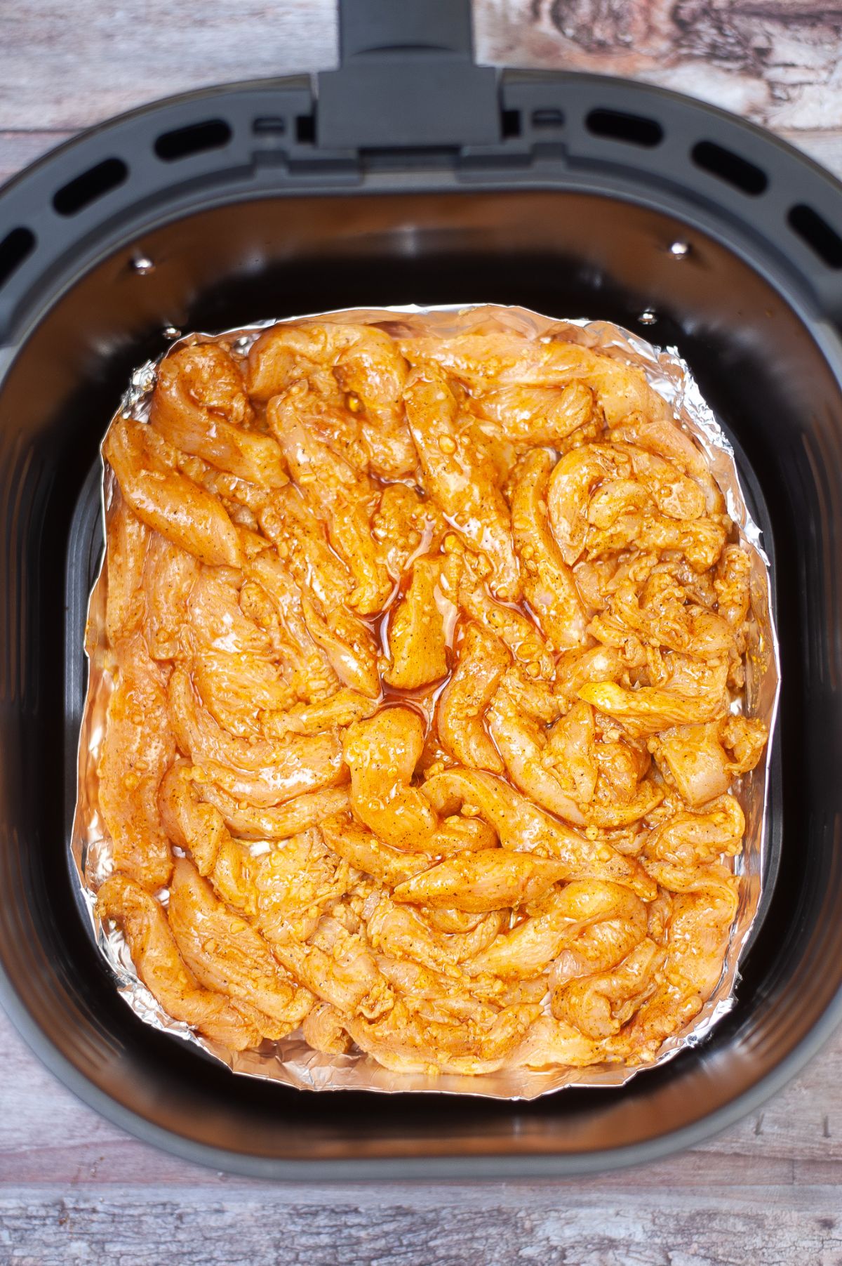 The Air Fryer is lined with aluminum foil tray and filled with marinated chicken.