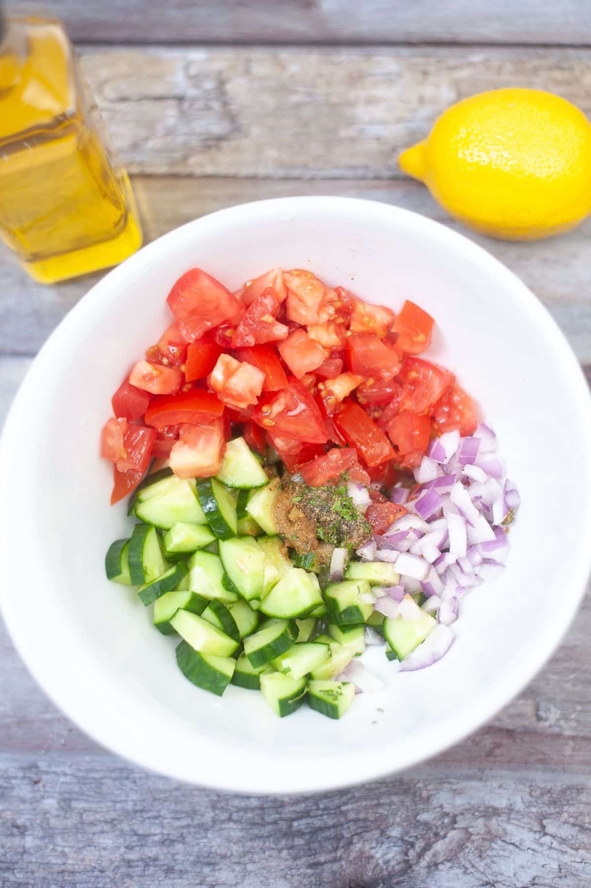 cucumber, tomatoes, onions and seasonings placed inside a small bowl.