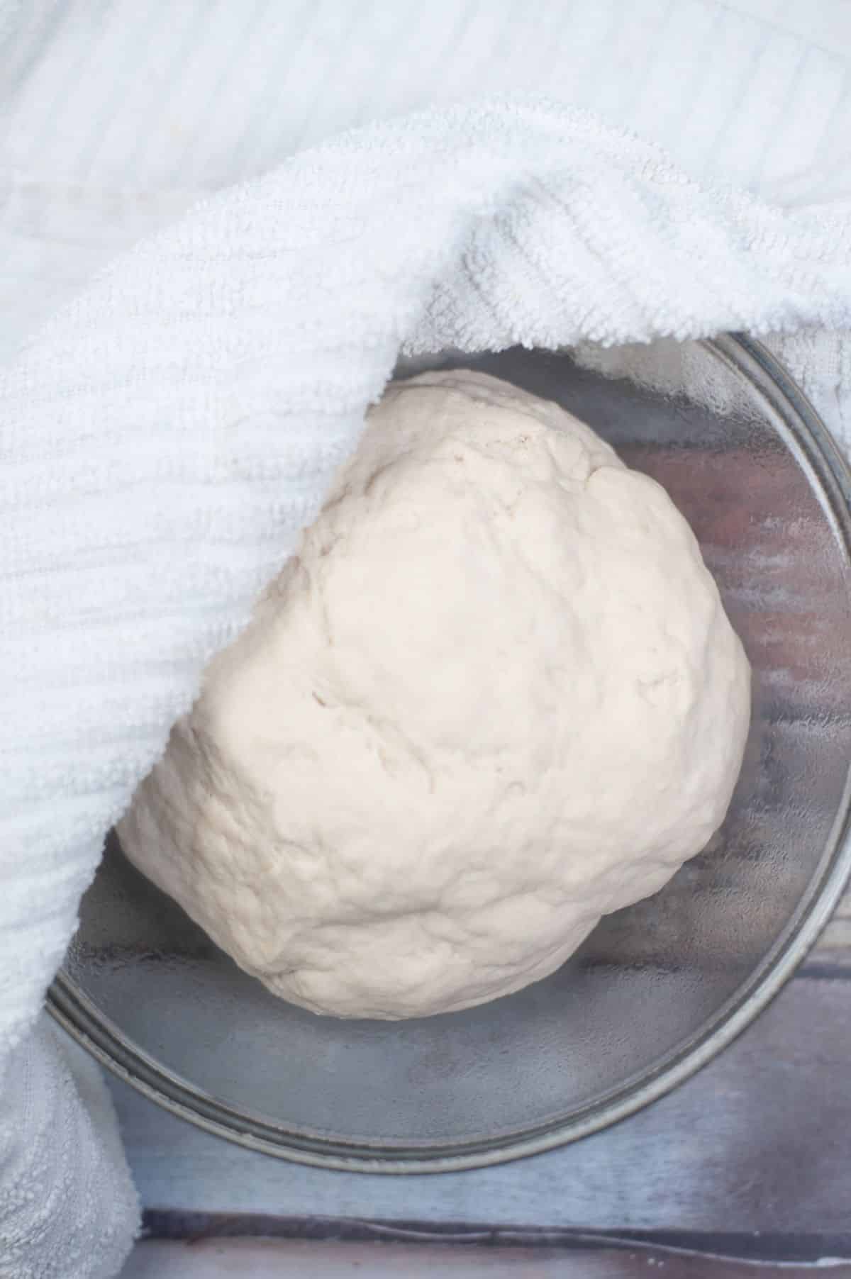 dough inside the mixing bowl with clean kitchen towel on the side.