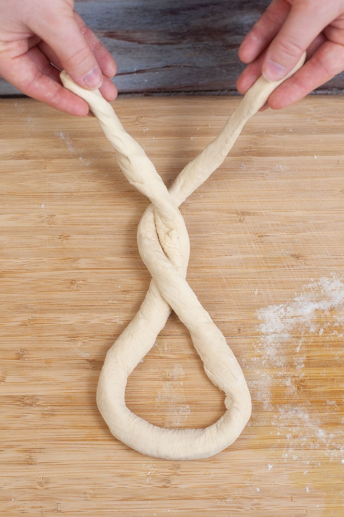 Pretzel dough is twisted by hand on a wooden chopping board.